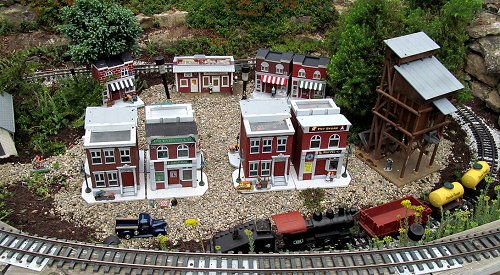 This photo was taken after our second open house, when I was running one of my more beat-up locomotives for the fun of it.  Most of the buildings in this photo were originally elsewhere, but they've been dislocated by a rapidly growing fir tree.  Click for bigger photo.